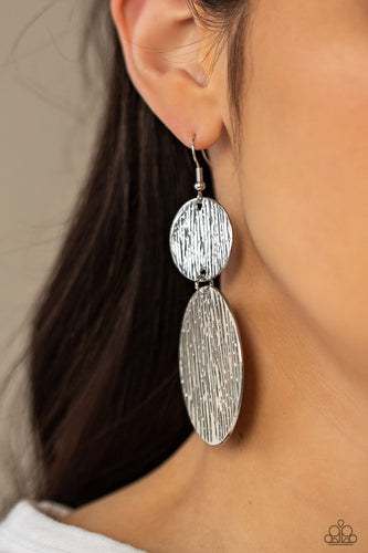 Embossed in tactile linear patterns, two mismatched silver discs link into a glistening lure. Earring attaches to a standard fishhook fitting.